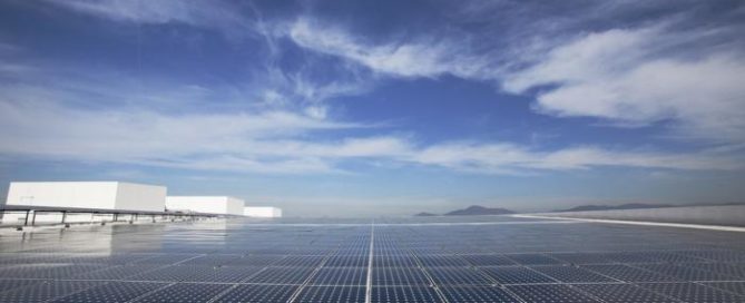 Large array of solar panels on a rooftop under a bright blue sky, showcasing renewable energy production.