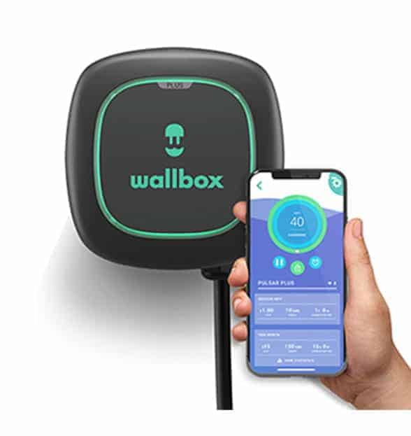 Wallbox electric vehicle charger with a black and green design, shown alongside a hand holding a smartphone displaying the Wallbox app interface for monitoring and configuring charging settings.