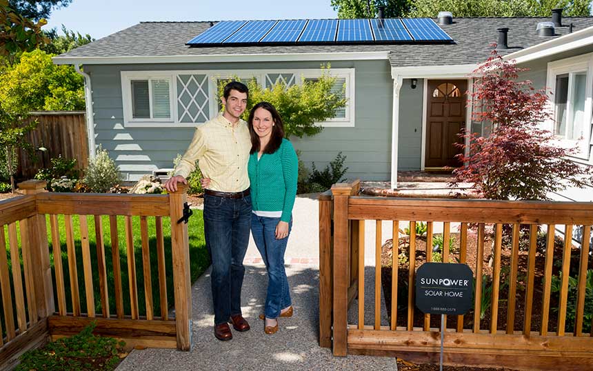Happy homeowners standing in front of their house with solar panels installed on the roof