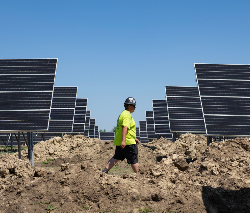 Ground-mounted solar array installation with technician inspecting solar field Ground-mounted solar array installation with technician inspecting solar field