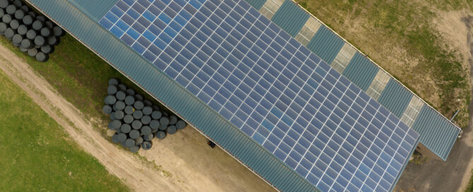 Aerial view of blue photovoltaic solar panels mounted on farm building roof for producing clean ecological electricity. Production of renewable energy concept