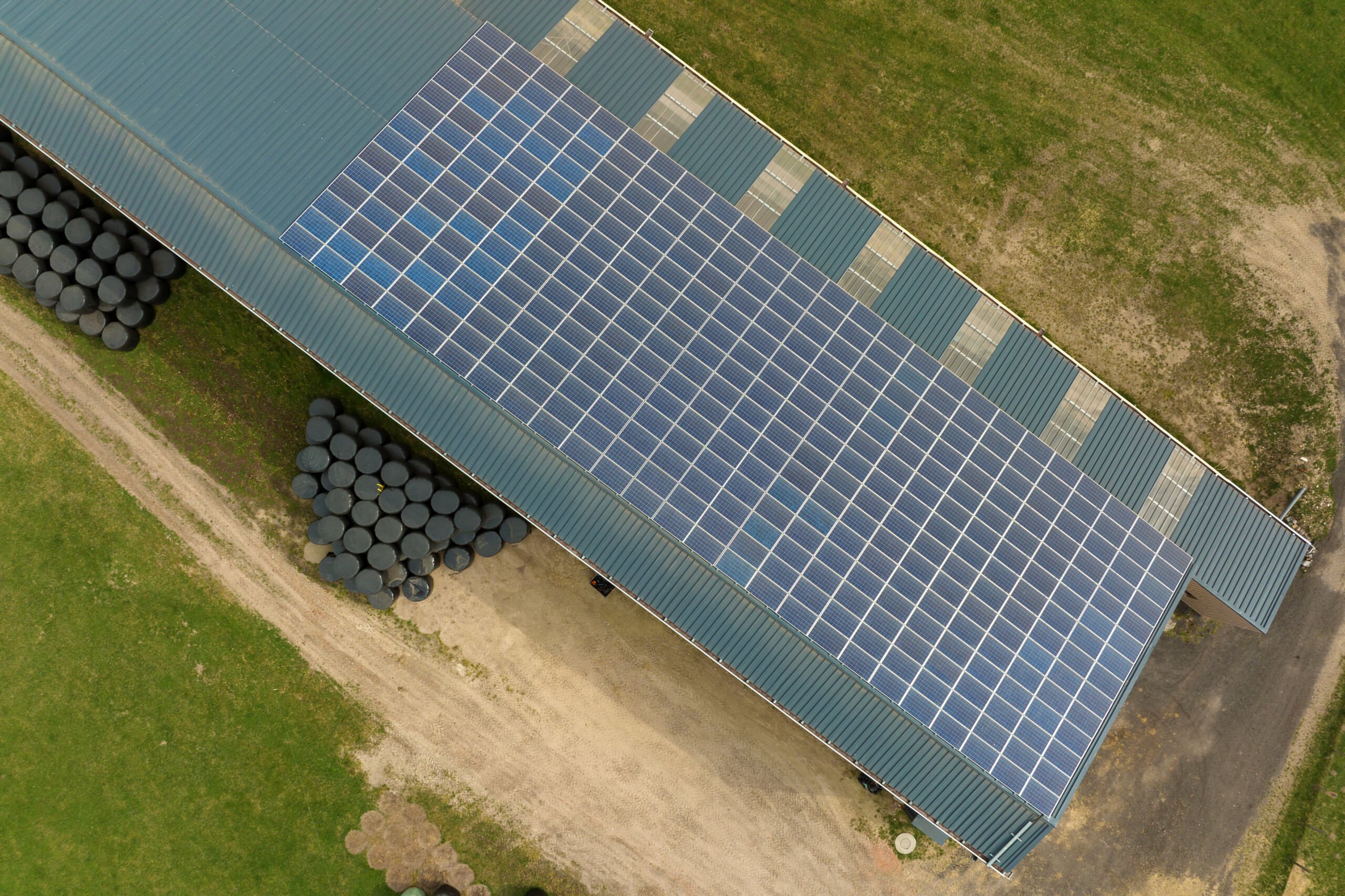 Aerial view of blue photovoltaic solar panels mounted on farm building roof for producing clean ecological electricity. Production of renewable energy concept