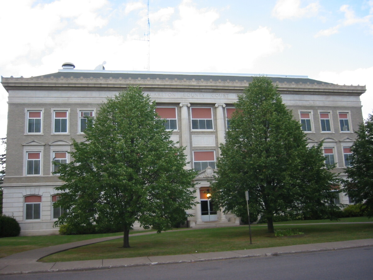 Front shot of the Carlton County Courthouse with two blooming trees in front of it during the day.