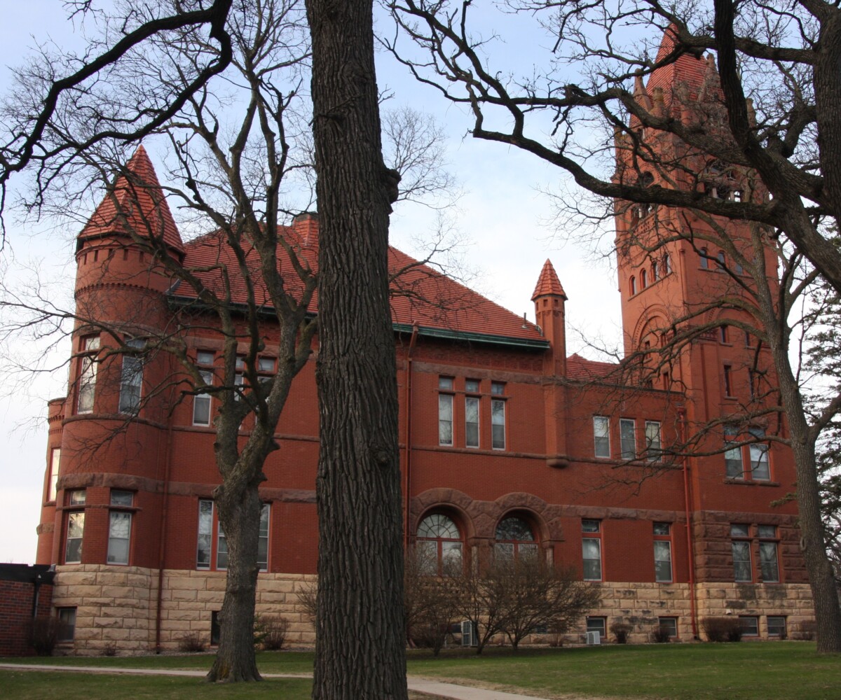 A side view of the Faribault County Courthouse during the day with trees in the forefront.