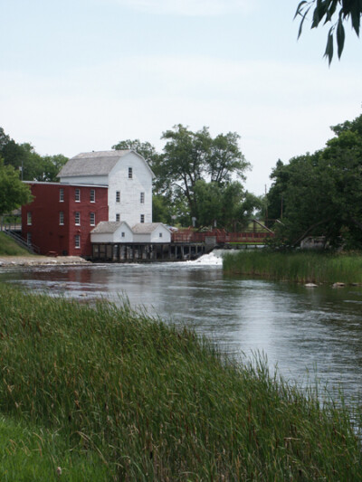 Shot of the Phelps Mill with a river and green grass in the forefront during the day. Shot of the Phelps Mill with a river and green grass in the forefront during the day.