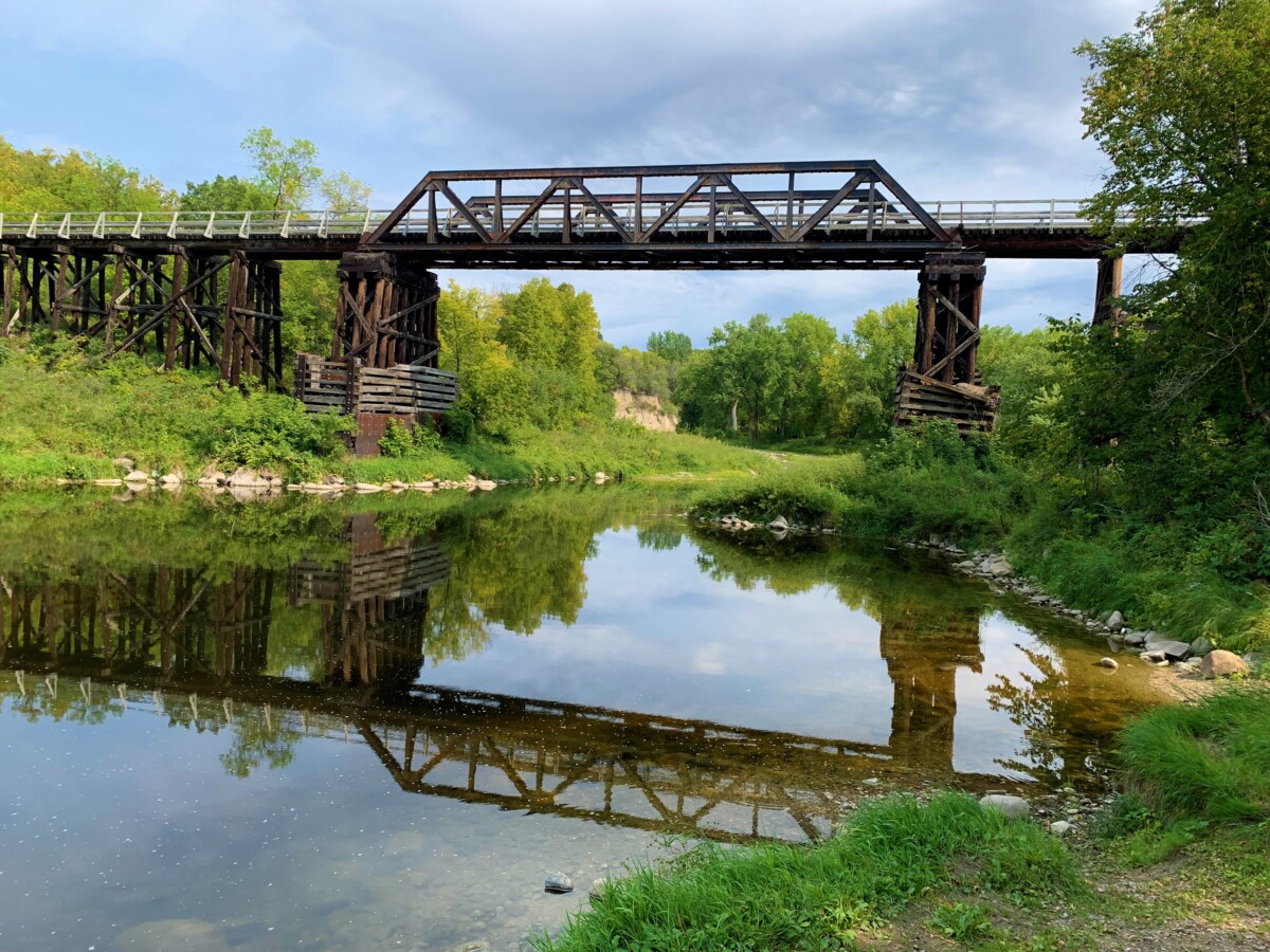 Shot of the Red Lake River with a bridge above it and greenery surrounding it during the day. Shot of the Red Lake River with a bridge above it and greenery surrounding it during the day.
