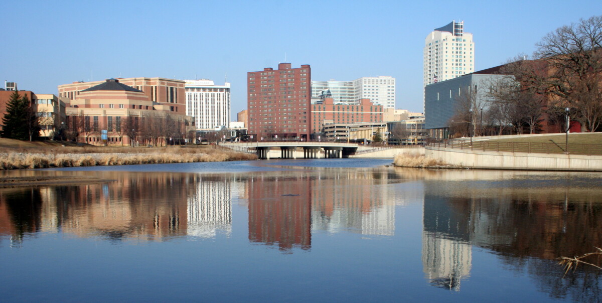 View of buildings on the skyline of Rochester, Minnesota with water in the forefront during the day. View of buildings on the skyline of Rochester, Minnesota with water in the forefront during the day.