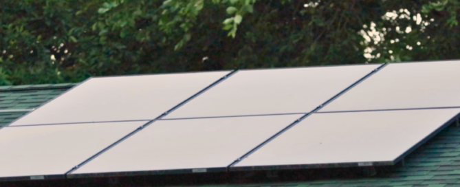 Close-up of high-efficiency solar panels installed on green shingle roof by Wolf River Electric, framed by leafy trees
