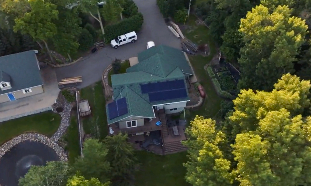 Aerial view of rural home with custom solar panel layout by Wolf River Electric, nestled among trees with visible garden and pond