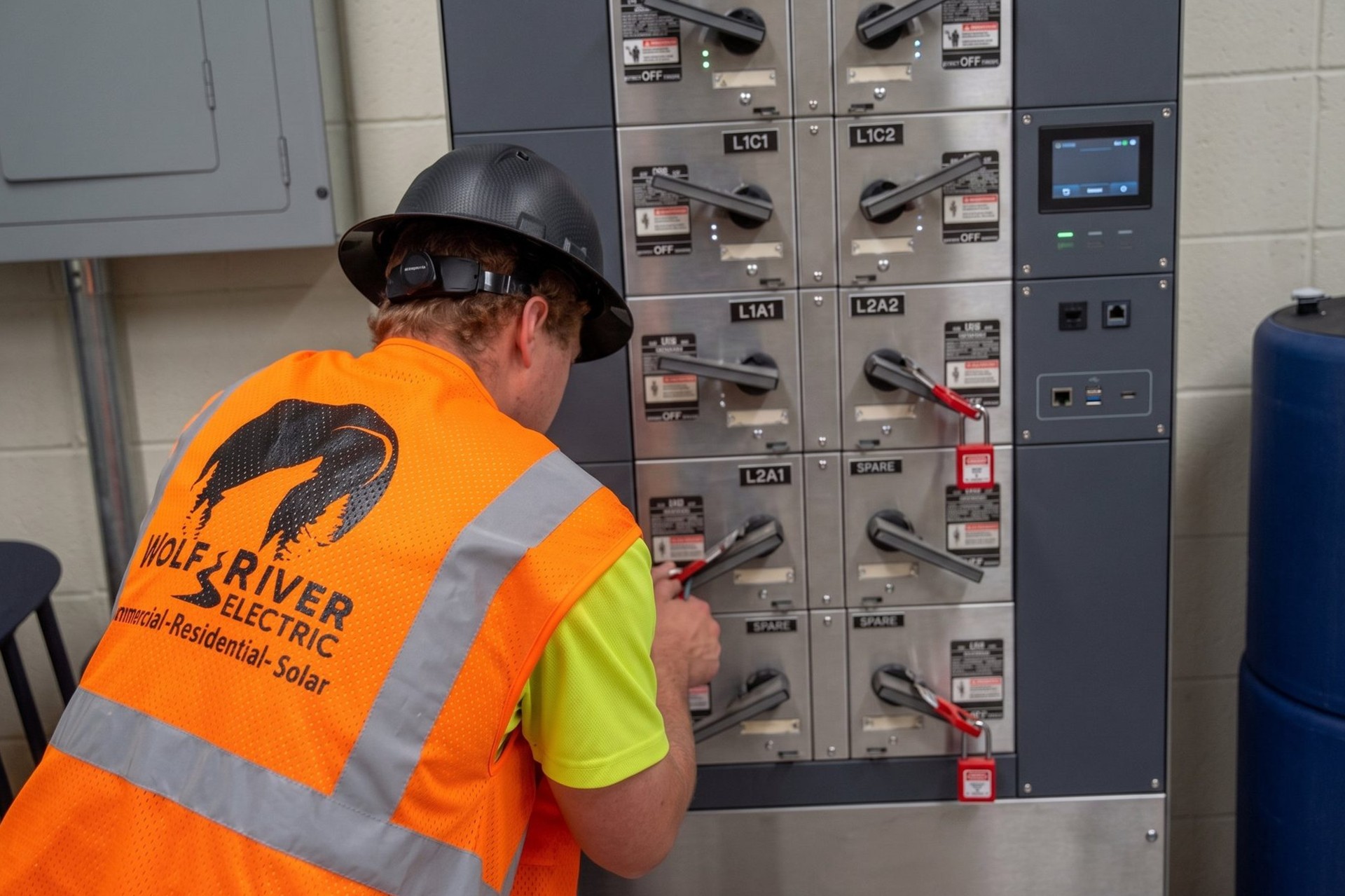 Electrician in a Wolf River Electric vest and hard hat working on commercial switchgear
