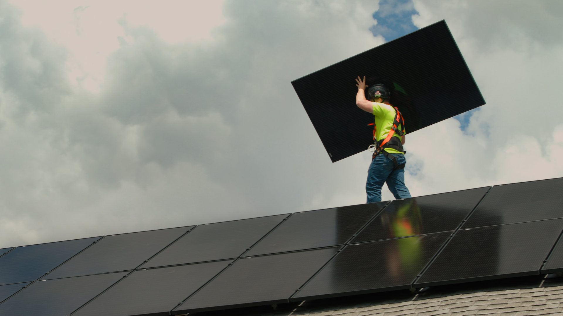 Wolf River Electric installer in a hard hat and harness carrying a black solar panel across a roof