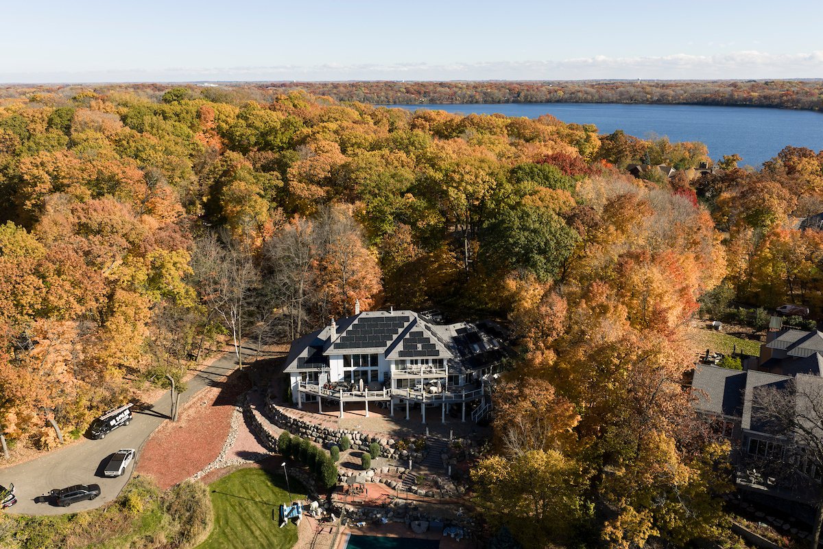 Aerial view of a home with rooftop solar among autumn trees by a lake, installed by Wolf River Electric