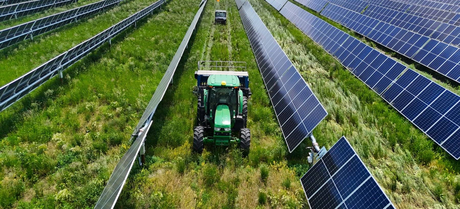Tractor working the ground between rows of solar trackers on a farm
