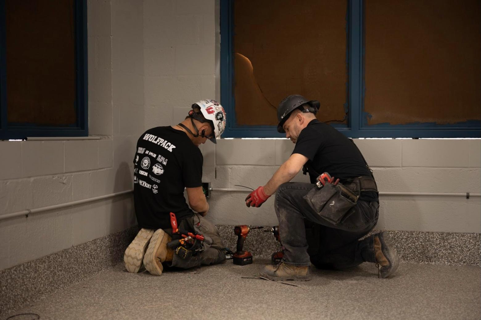 Two Wolf River Electric electricians in hard hats wiring conduit inside a commercial building